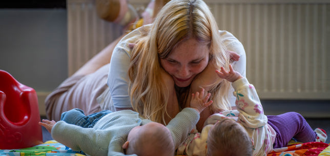 Woman watching two babies playing on a mat