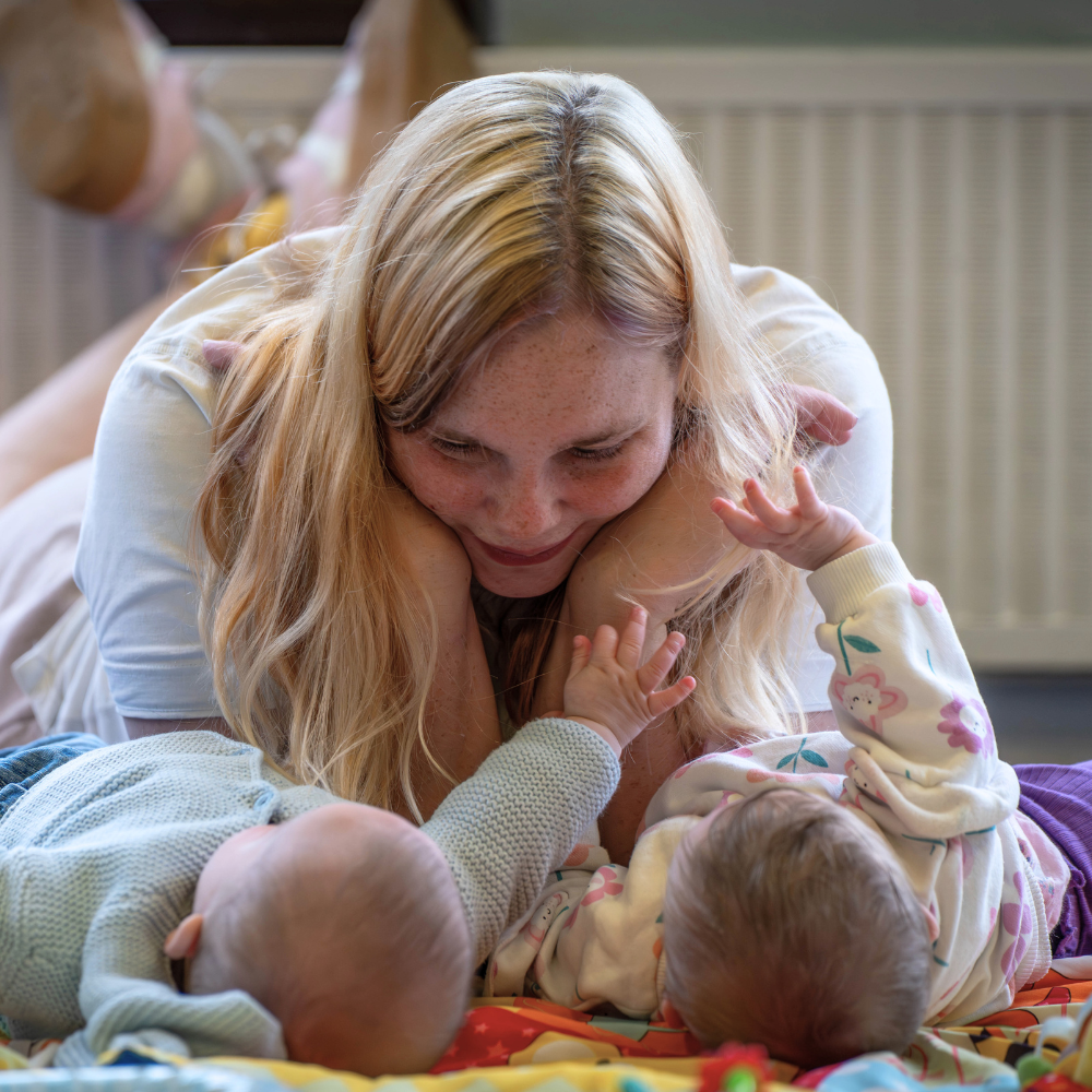 Woman watching two babies playing on a mat