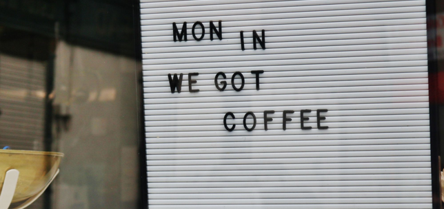 Board on a shop window that says 'Mon in we got coffee'