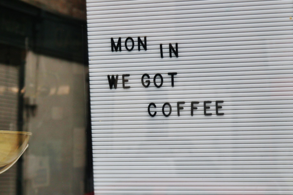 Board on a shop window that says 'Mon in we got coffee'