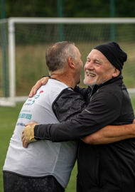 Two teammates celebrating with a hug during a walking football match.