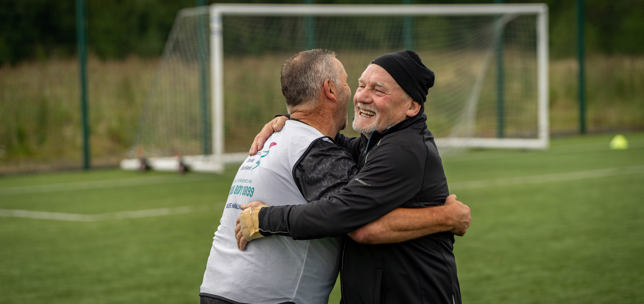 Two teammates celebrating with a hug during a walking football match.