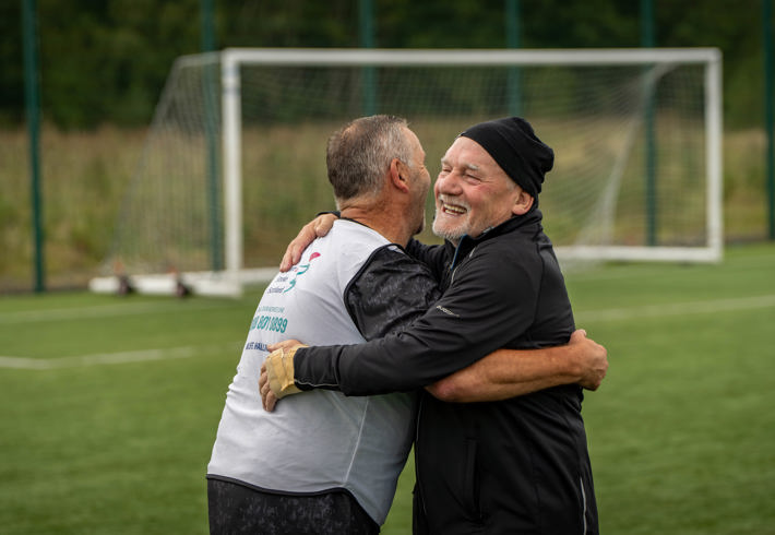 Two teammates celebrating with a hug during a walking football match.