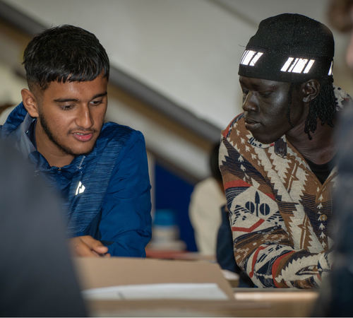 Two young adults in a classroom setting looking at information on paper together