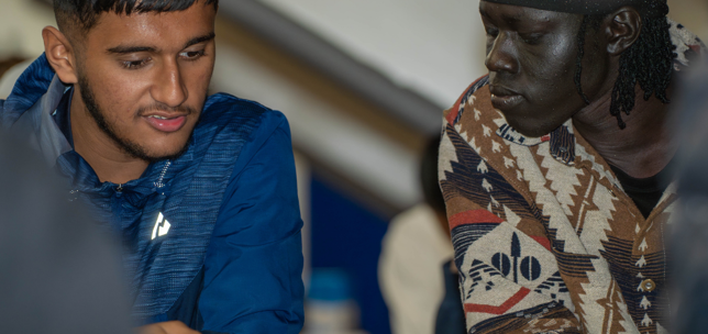 Two young adults in a classroom setting looking at information on paper together