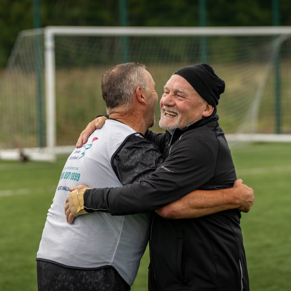 Two teammates celebrating with a hug during a walking football match