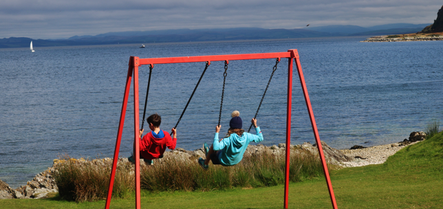 Two young children on swings by the sea